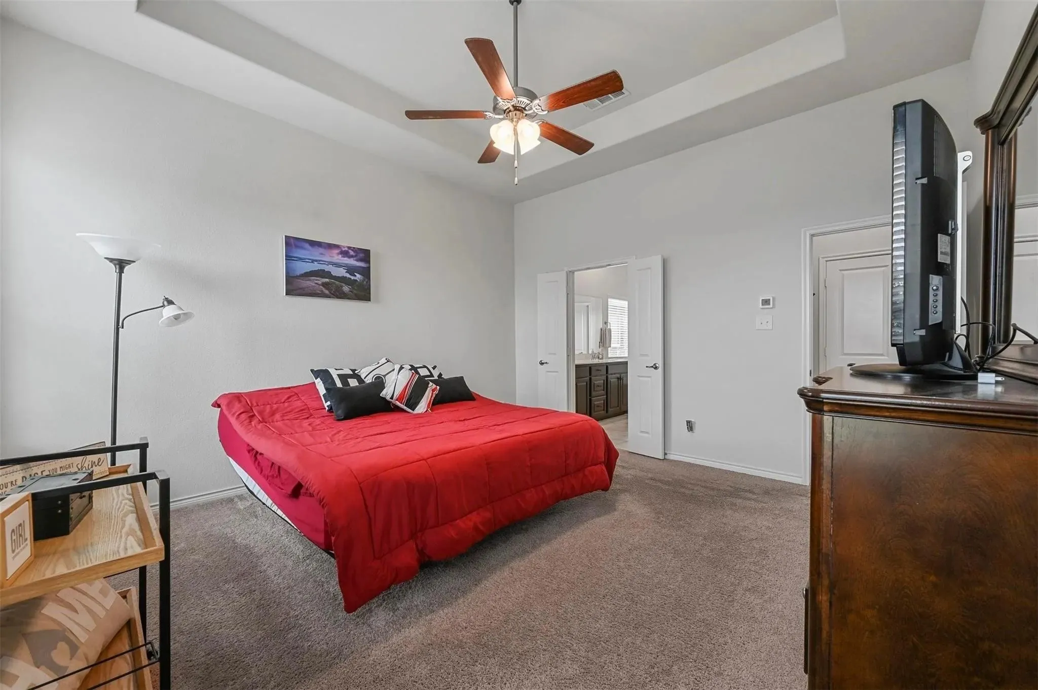 Tray ceiling with a ceiling fan, neutral carpeting, and double doors opening to an adjoining room