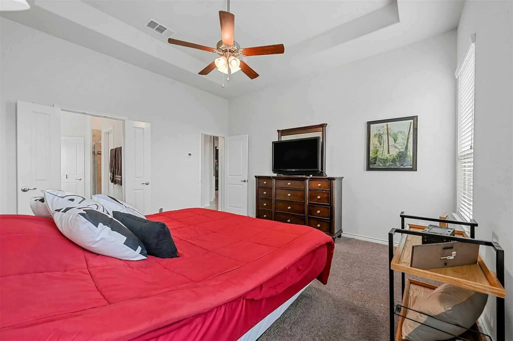 Tray ceiling with a ceiling fan, white paneled doors, and a window with blinds
