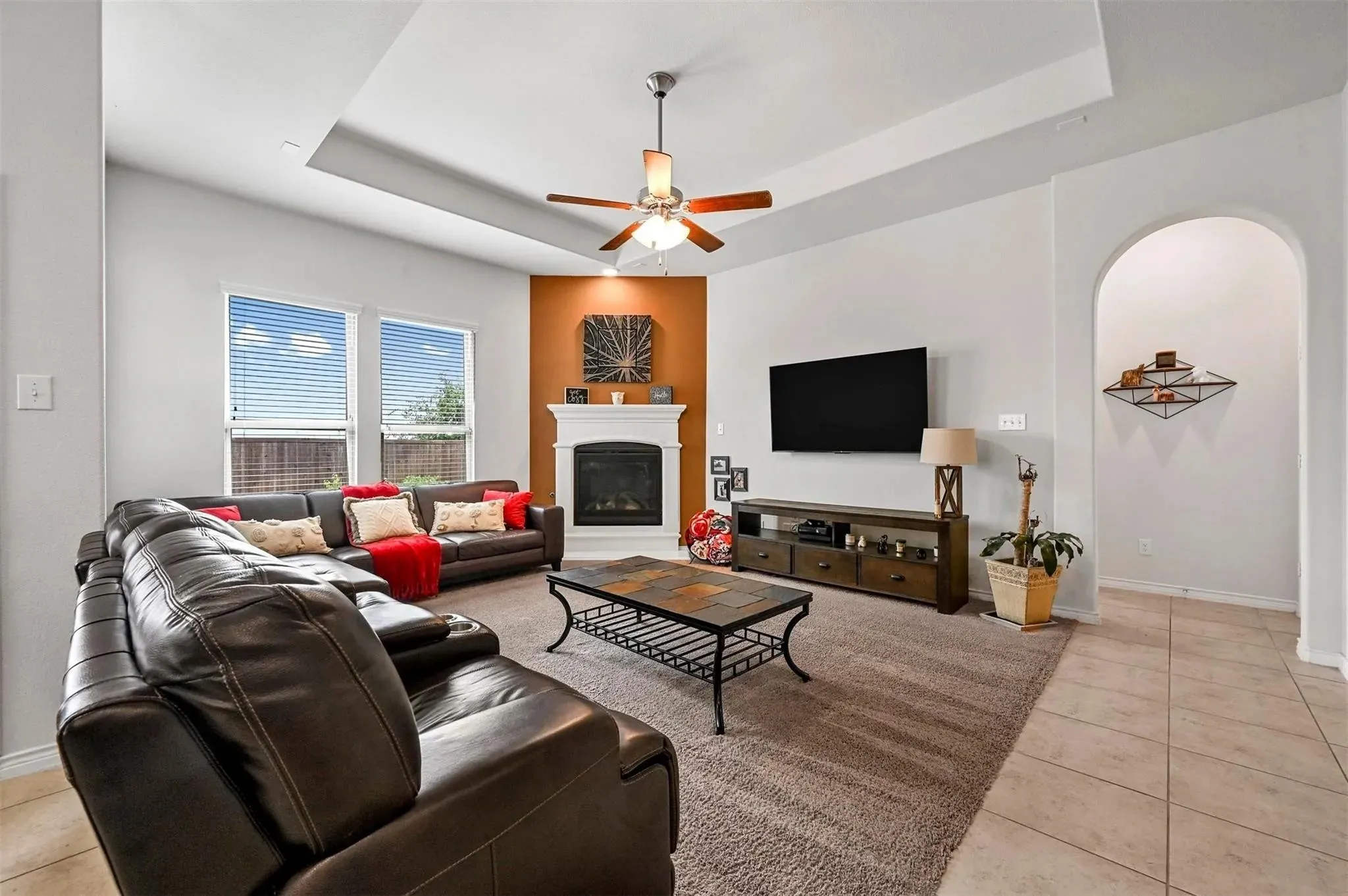 Living area featuring a tray ceiling, ceiling fan, and a built-in fireplace with white mantel