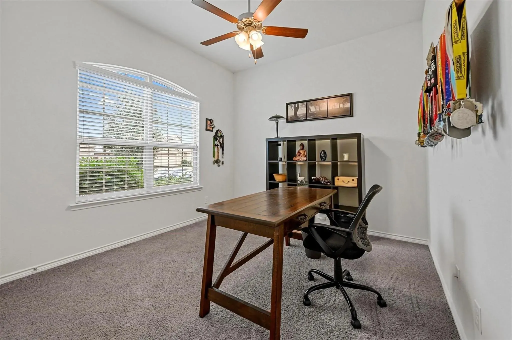 Arched window with blinds, ceiling fan with light fixture, neutral carpet, and white walls