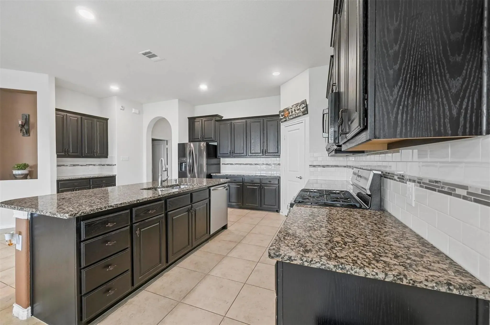 Kitchen featuring dark wood-finish cabinetry, granite countertops, tile flooring, stainless steel appliances, and an expansive center island with an undermount sink