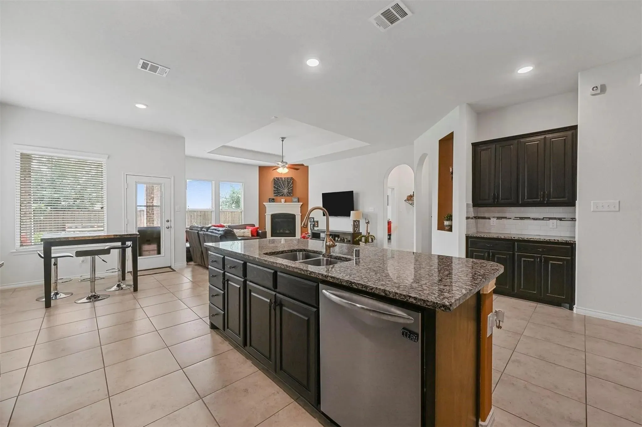 Kitchen with tile flooring, island with integrated sink, stainless steel dishwasher, and granite-style countertop