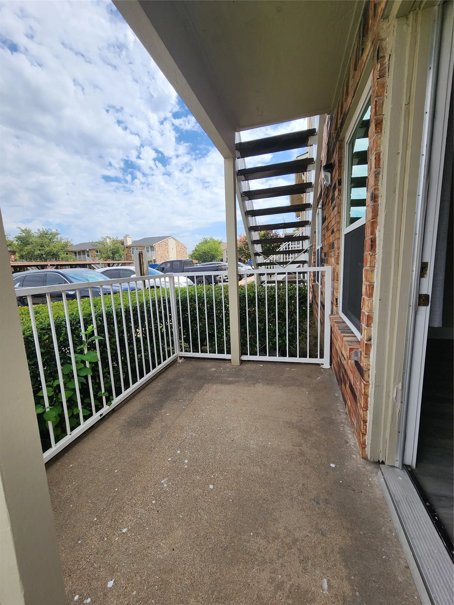Covered outdoor patio with a concrete surface, white metal railing, and brick exterior wall