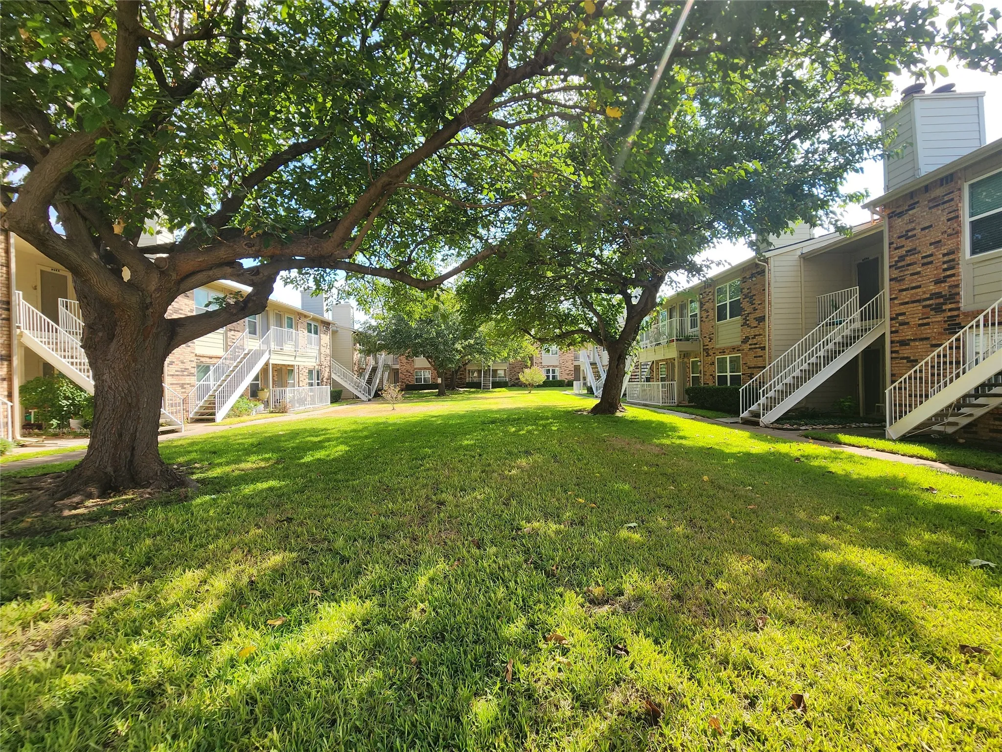 Expansive green space featuring mature trees, manicured lawn, and multi-story buildings with brick and siding exteriors