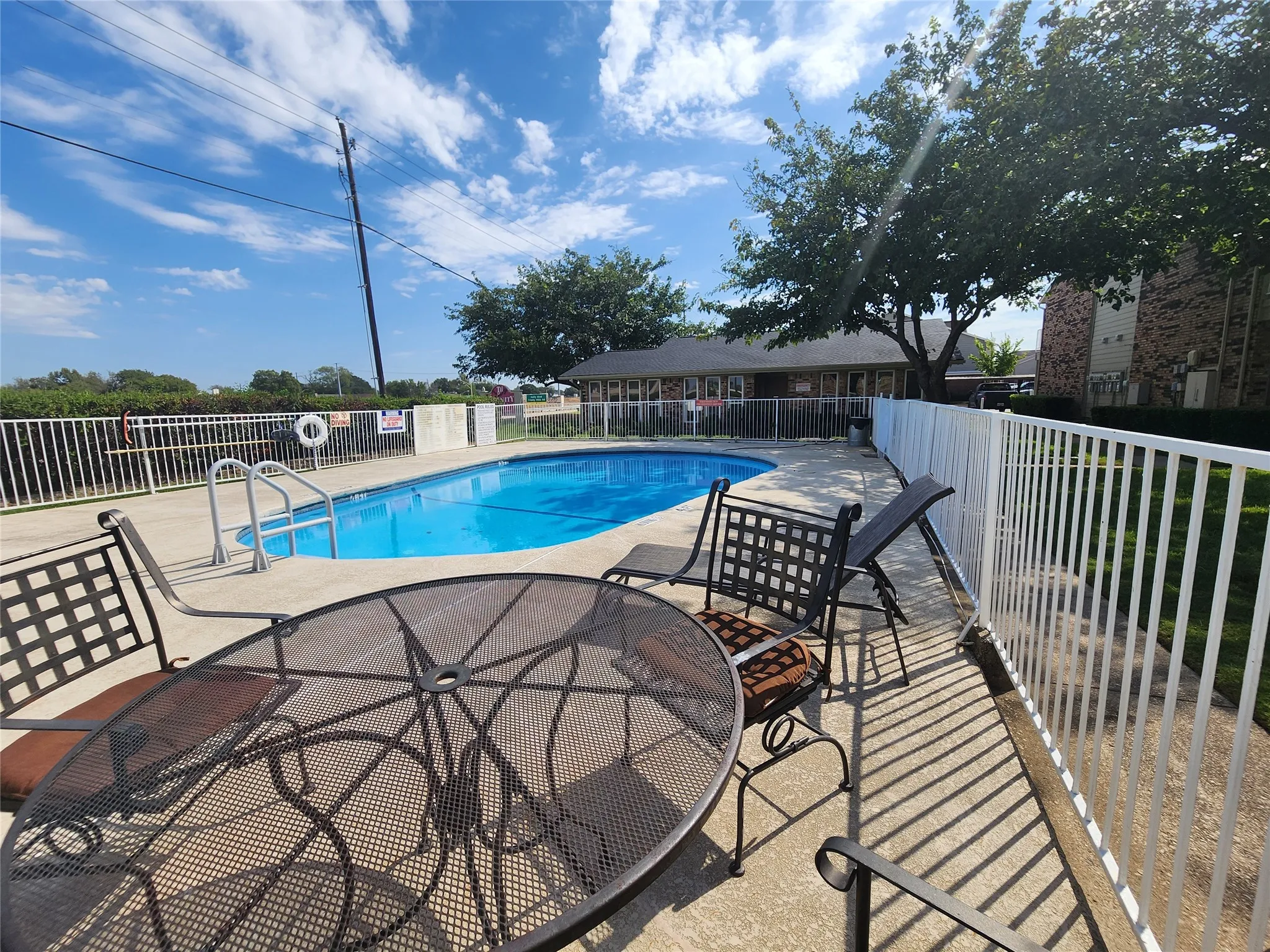 Fenced swimming pool with concrete decking, perimeter fencing, and mature trees