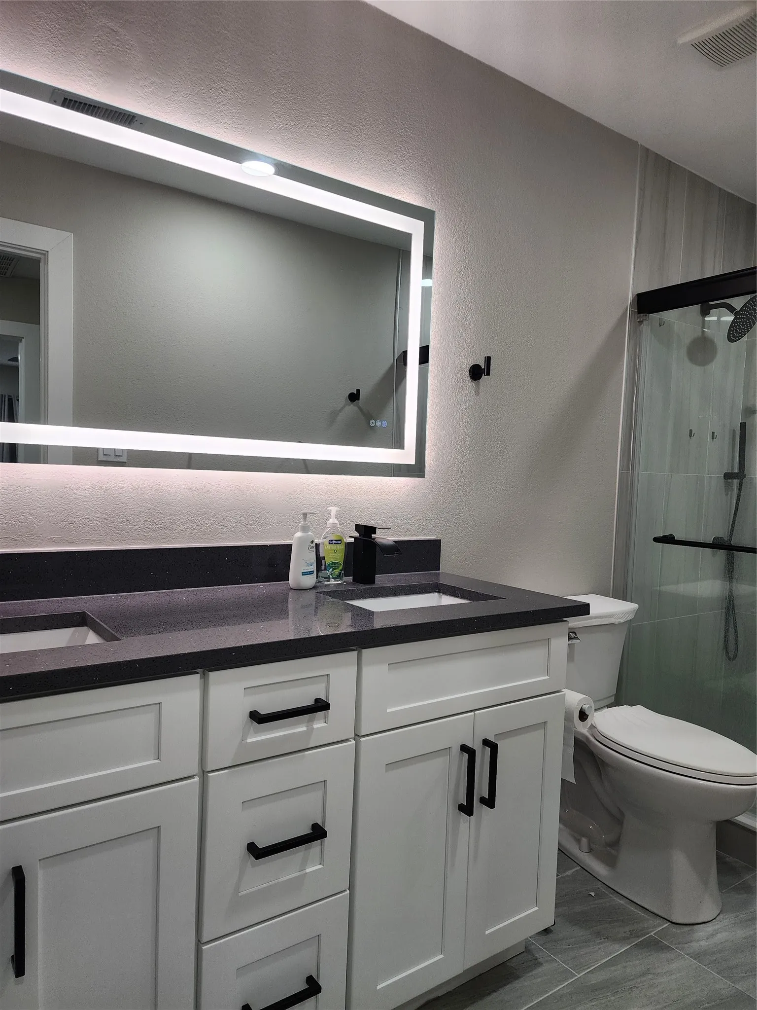 Dual vanity with white cabinetry, dark countertop, and matte black hardware