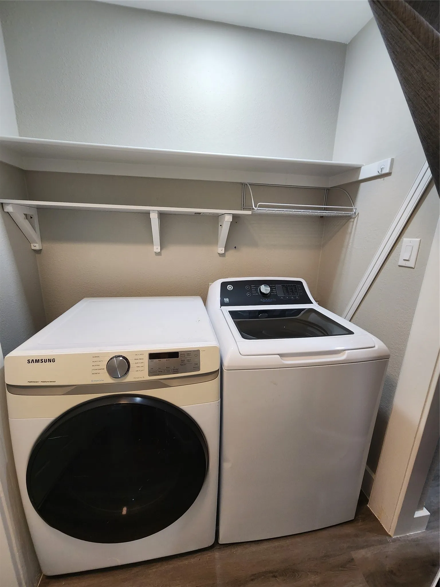 Laundry area featuring a built-in shelf, hanging rod, and wood-finish flooring