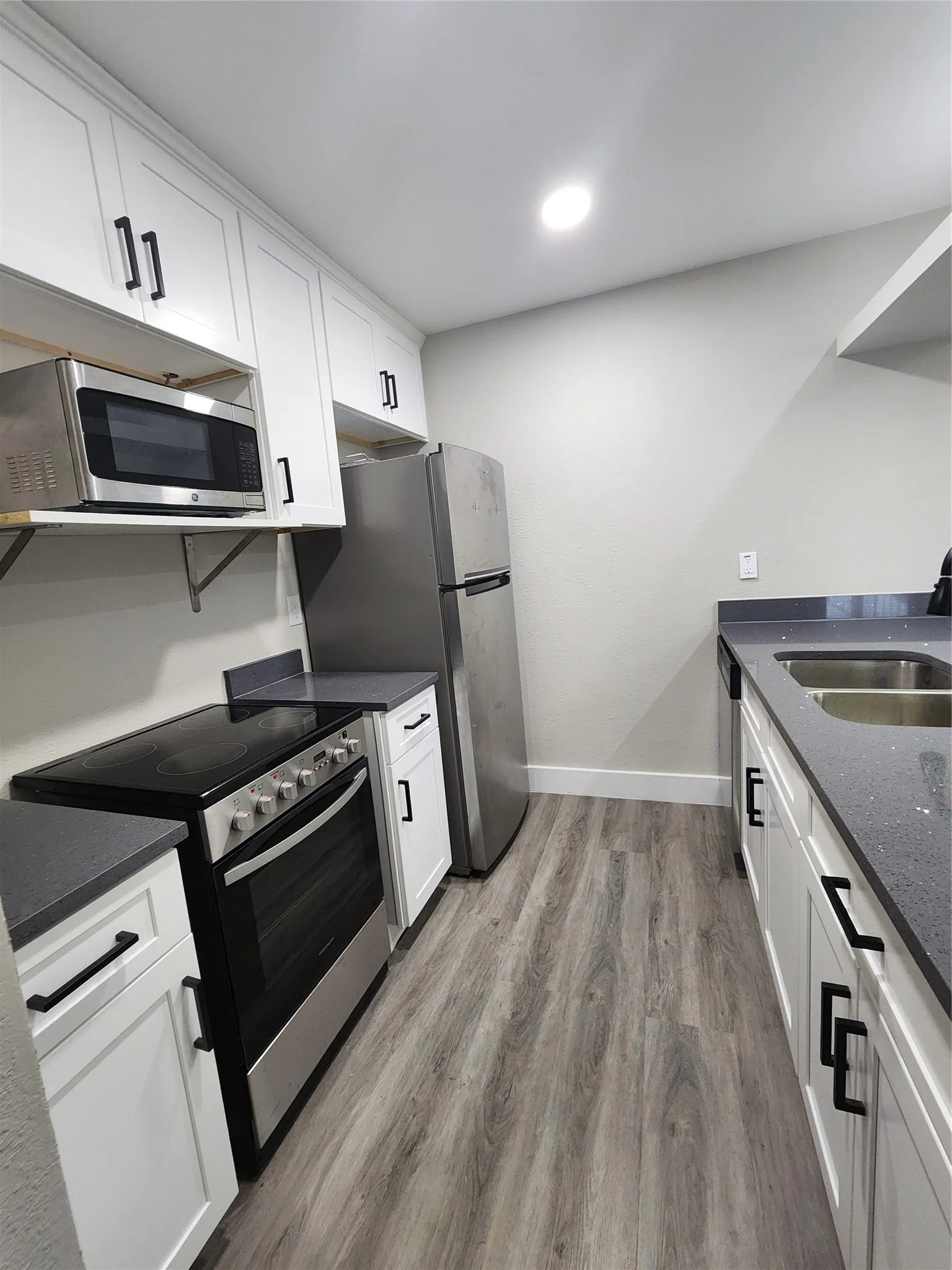 White cabinetry with black hardware, wood-finish flooring, dark countertops, and stainless steel appliances