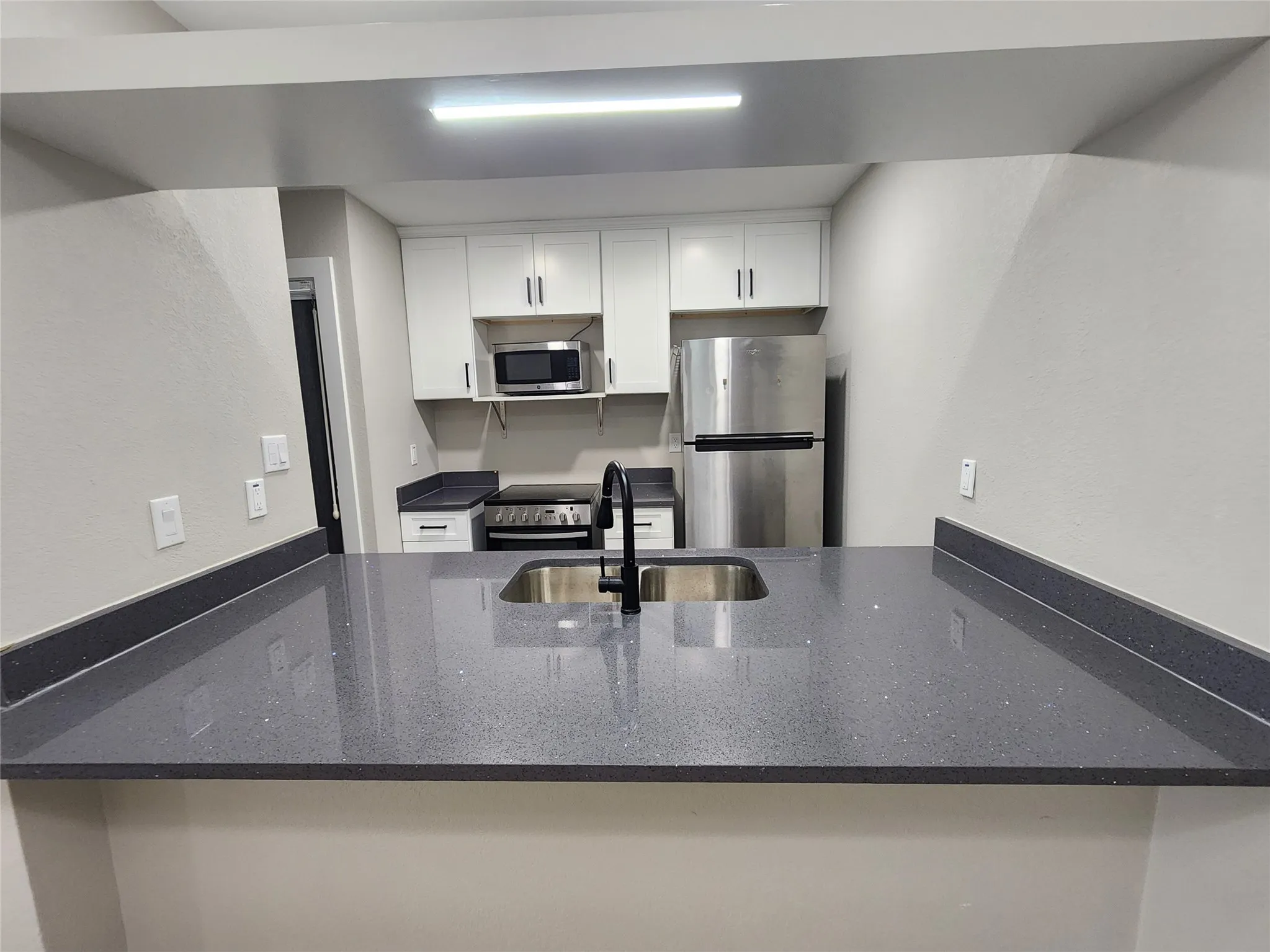Kitchen featuring white cabinetry, dark speckled countertops, a stainless steel refrigerator, stainless steel microwave, and a black gooseneck faucet with an undermount sink