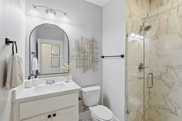 Glass-enclosed shower with floor-to-ceiling tile surround, single vanity with integrated sink and chrome fixtures, arched mirror, and contemporary wall-mounted light fixture