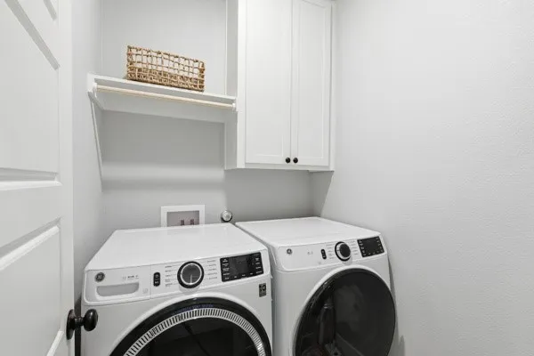 Dedicated laundry space featuring white shaker-style cabinetry, open shelving with a hanging rod, and light-toned wall finishes
