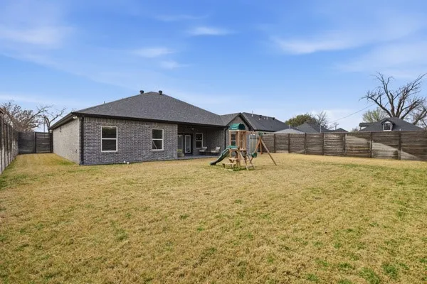 Expansive backyard with a full privacy fence, brick exterior, and covered patio area