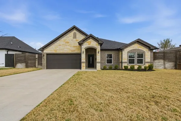 Brick and stone façade with arched entry, attached two-car garage, and established front landscaping