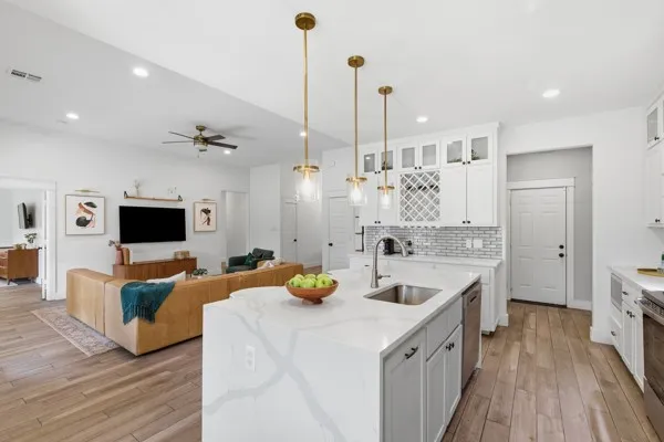 Open-concept living space featuring wood-finish flooring, a kitchen island with a sink, white cabinetry with glass inserts, and modern pendant lighting