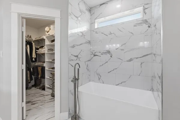 Freestanding soaking tub with floor-mounted faucet, white and gray patterned tile shower surround, and a clerestory window