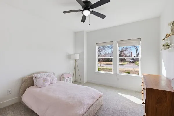 Recessed lighting, ceiling fan, two windows with roller shades, and light gray carpeting