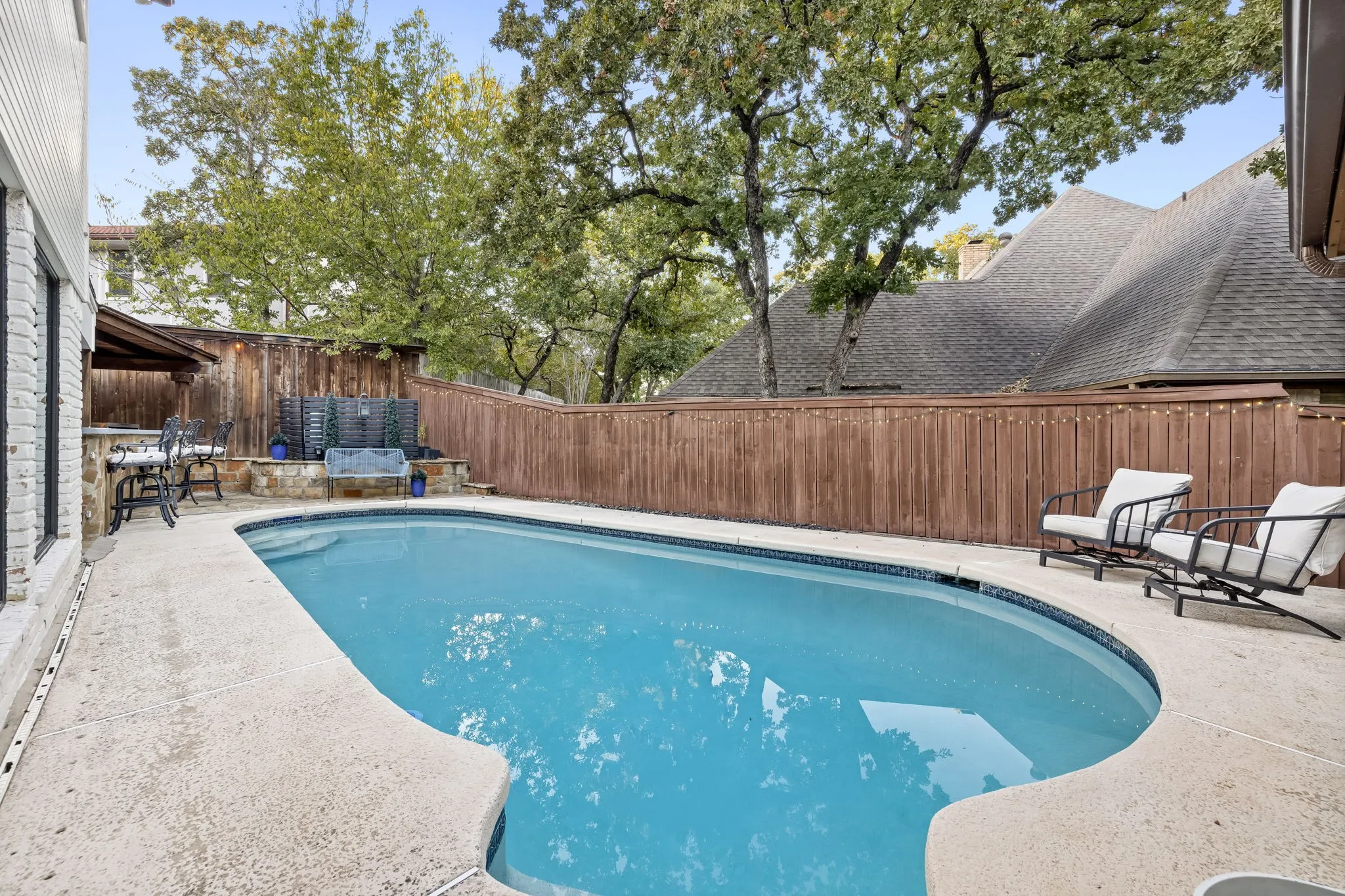 In-ground swimming pool with a concrete surround, wood privacy fencing, and an adjacent covered patio area