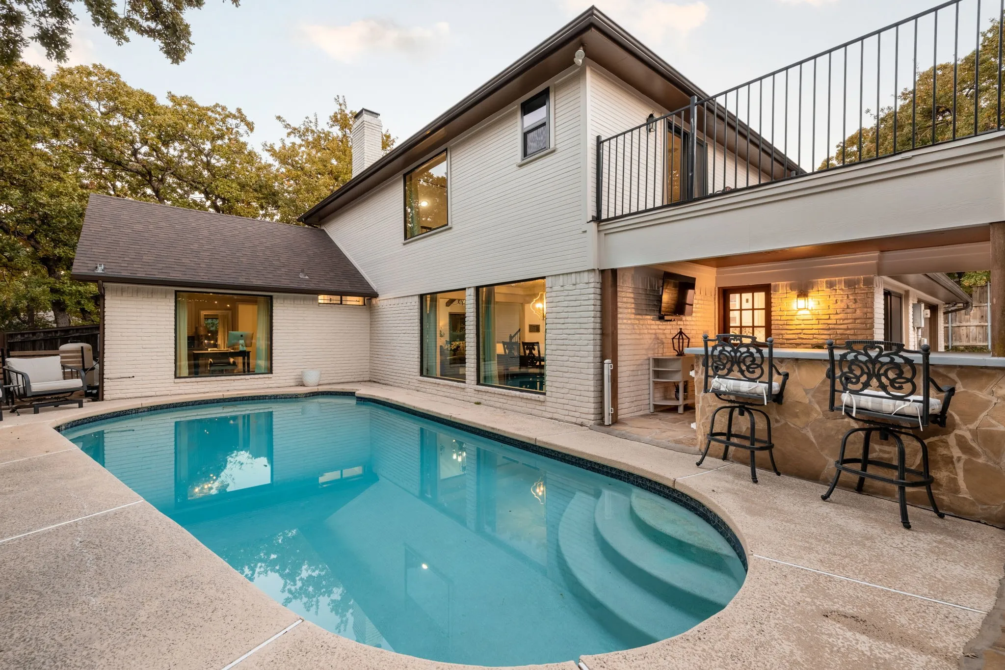 Exterior featuring a swimming pool, integrated outdoor bar, upper-level balcony with metal railing, and a brick facade
