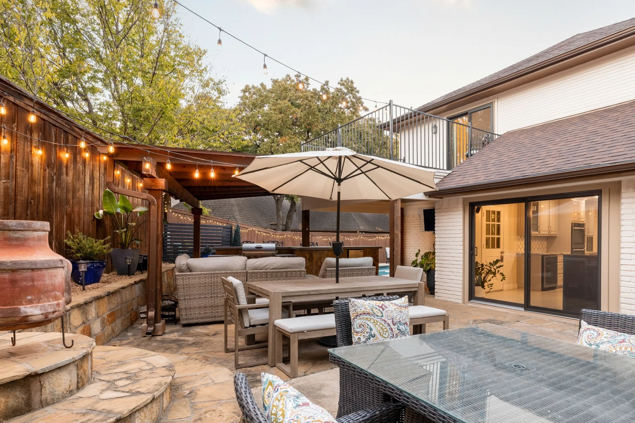 Stone patio with a wood pergola, built-in outdoor kitchen, and a second-story balcony
