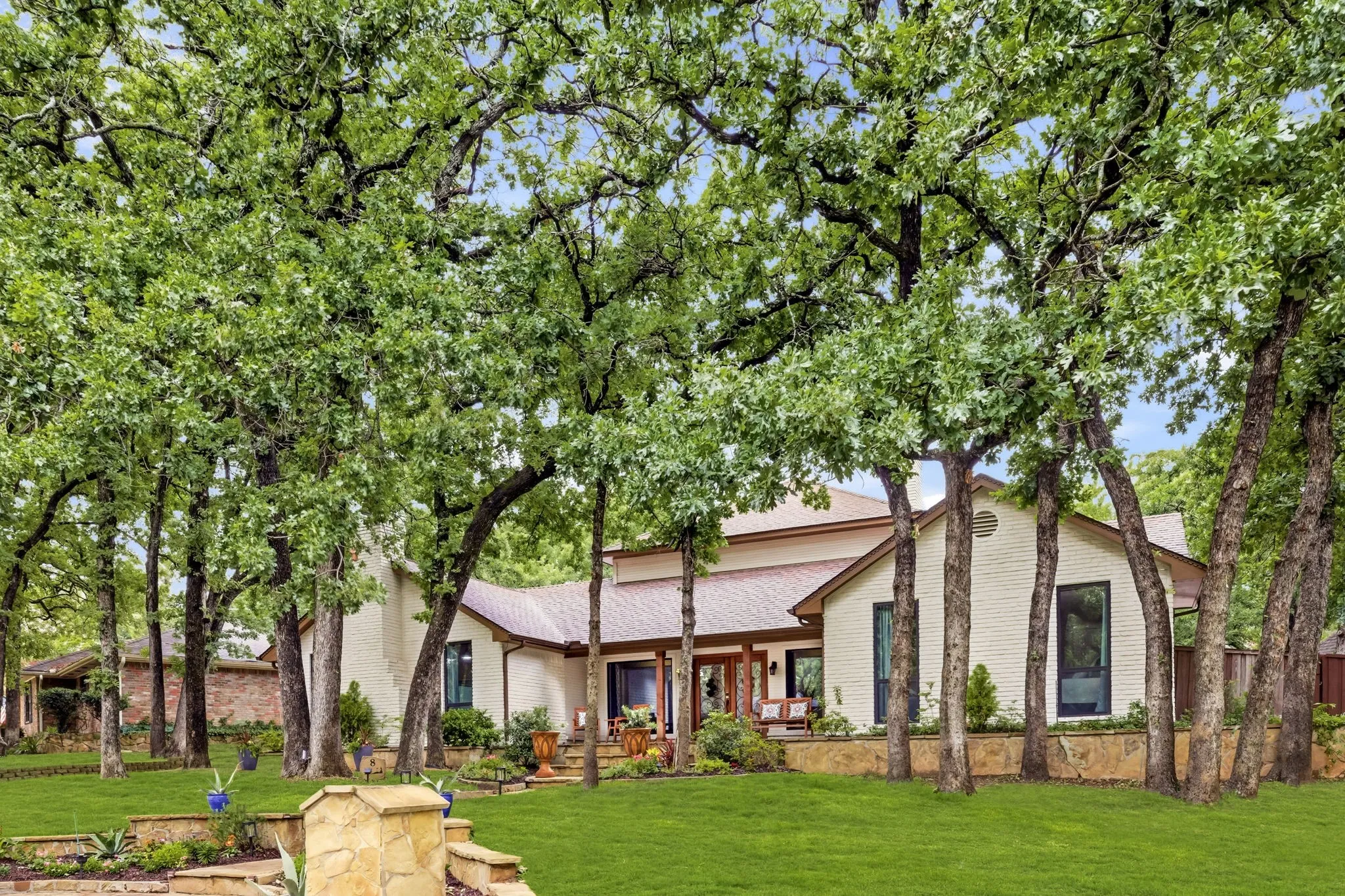 Exterior featuring a brick facade, pitched roofing, and multiple mature trees