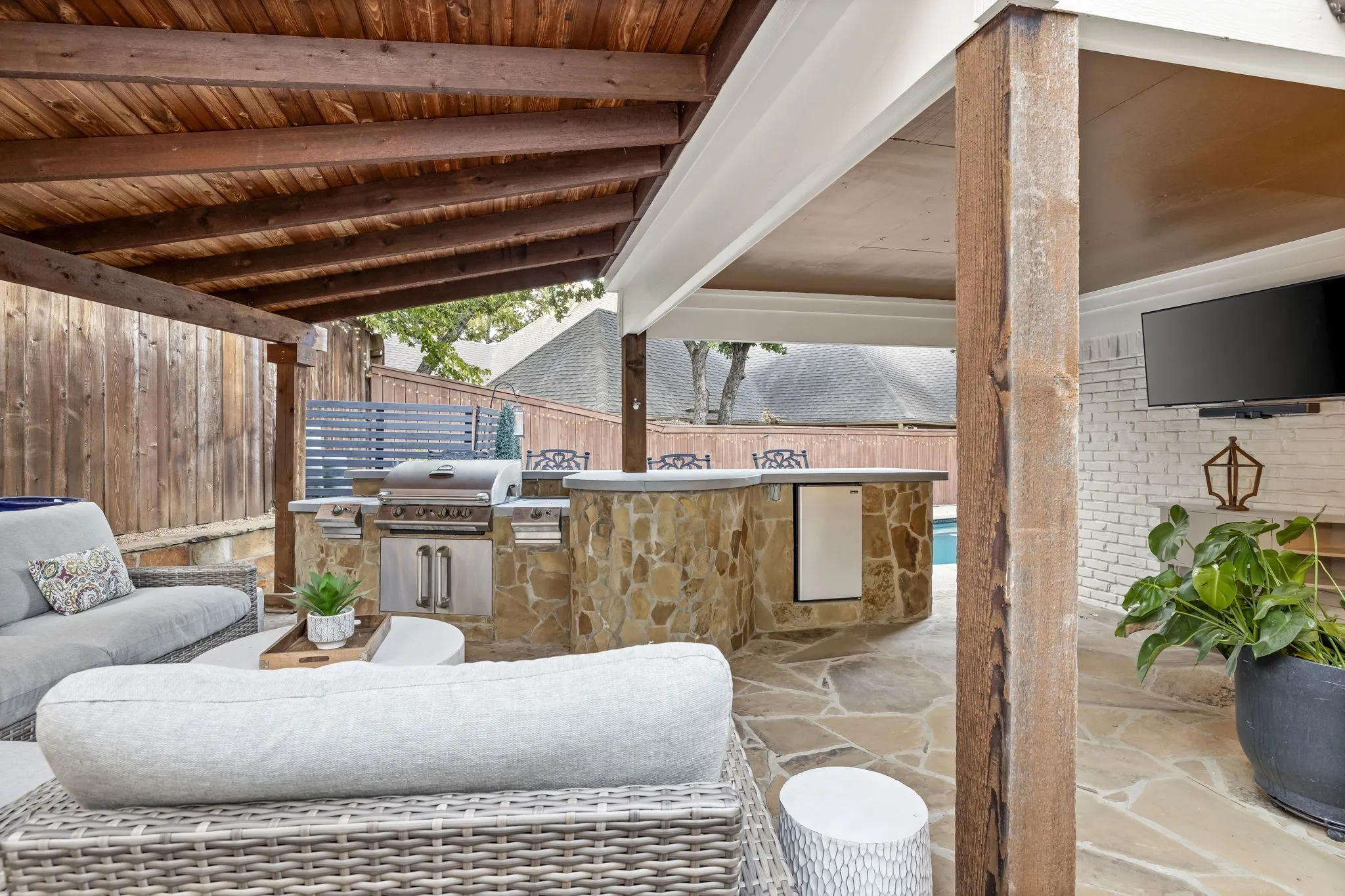 Expansive covered patio featuring a wood beam ceiling, flagstone flooring, a built-in outdoor kitchen with stainless steel appliances, and an outdoor bar with a built-in beverage refrigerator