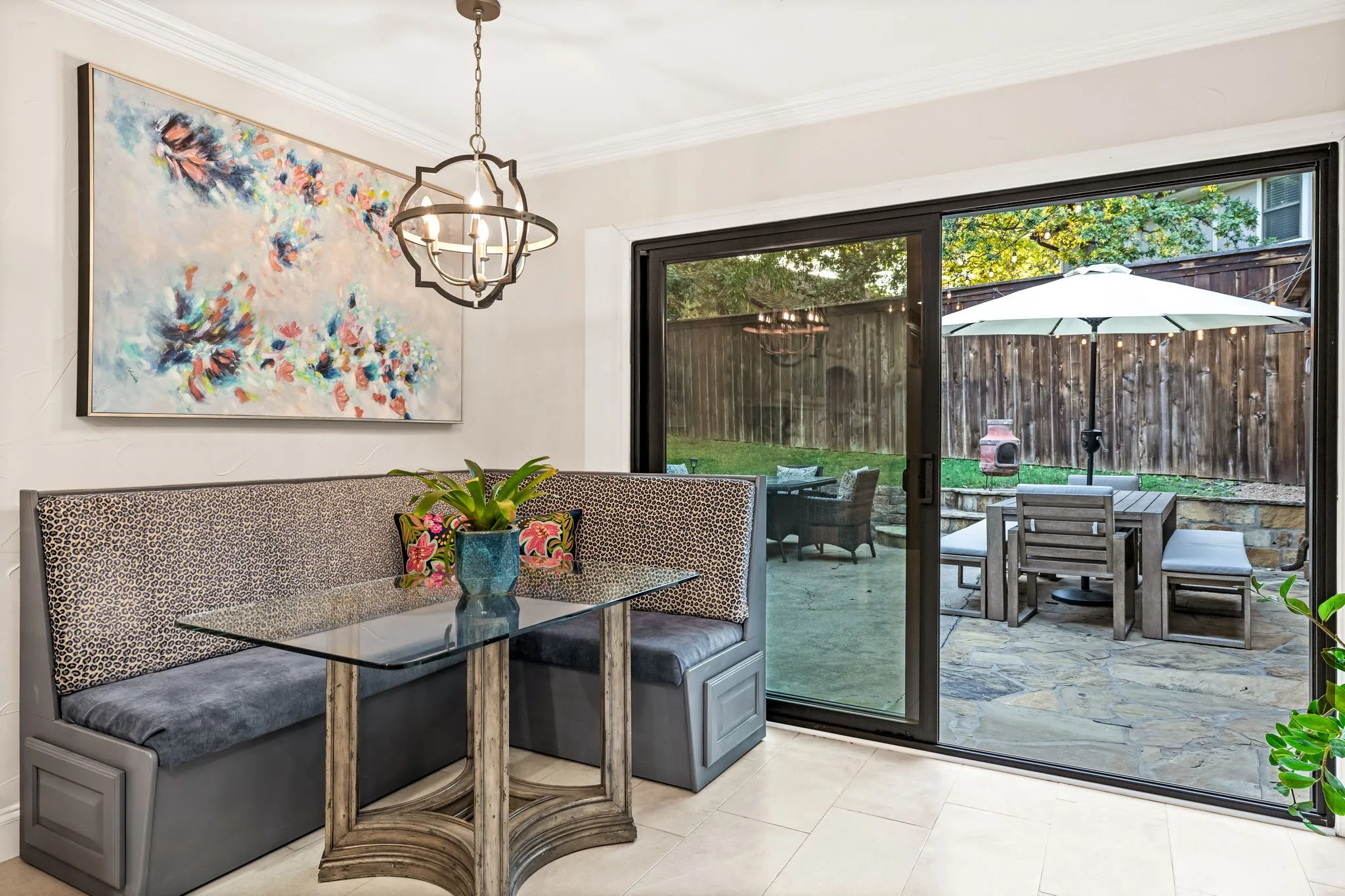 Built-in banquette seating with upholstered cushions, glass-top table, and an overhead orb-style chandelier