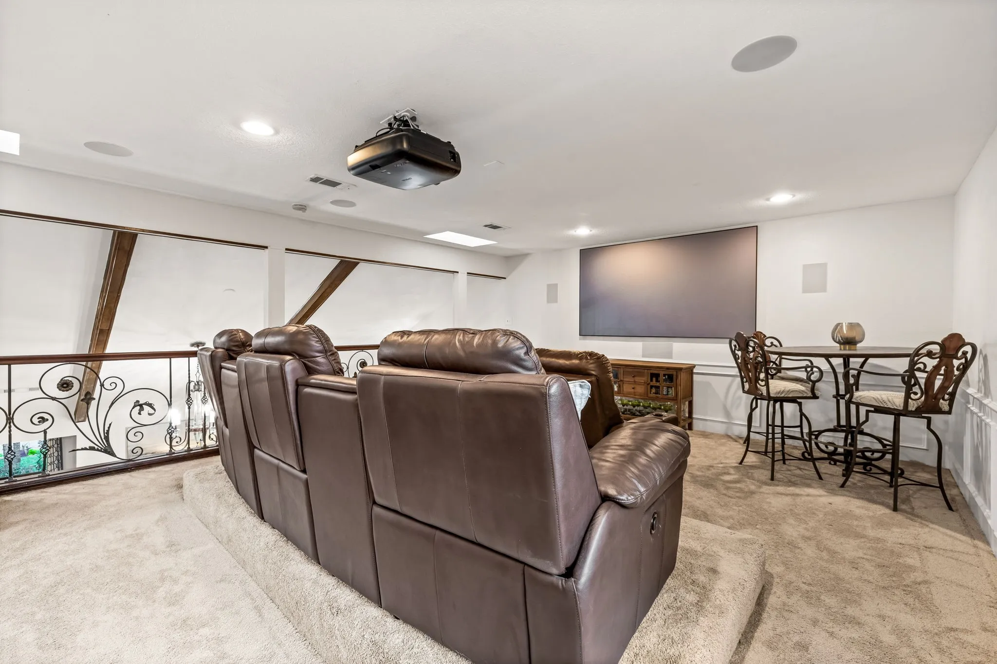 Entertainment space featuring a large projection screen, built-in ceiling speakers, recessed lighting, and an ornamental metal railing