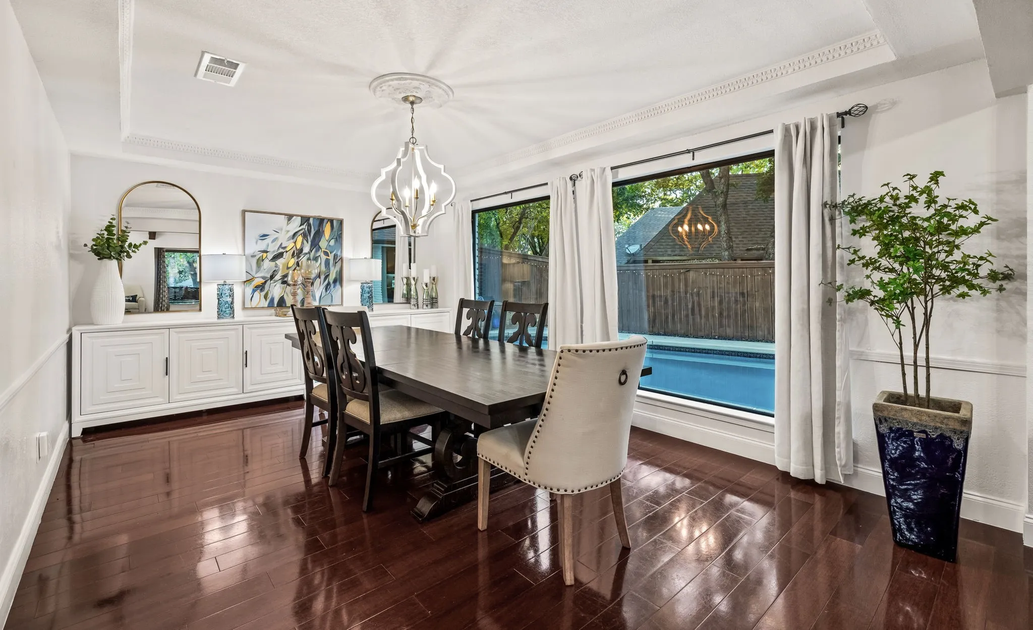 Hardwood-finish flooring, recessed ceiling with decorative molding, chandelier with white finish, built-in white buffet cabinetry, and large windows