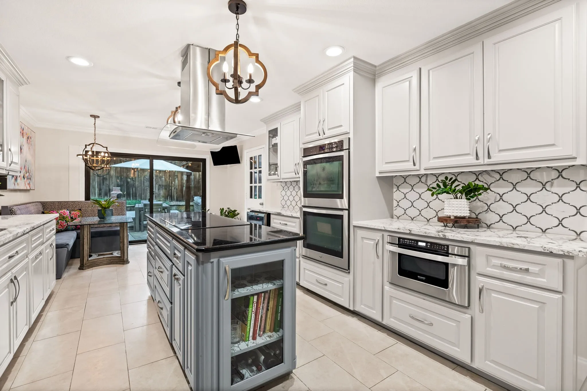Gourmet kitchen featuring a central island with black countertop, stainless steel appliances, white cabinetry with crown molding, and patterned tile backsplash