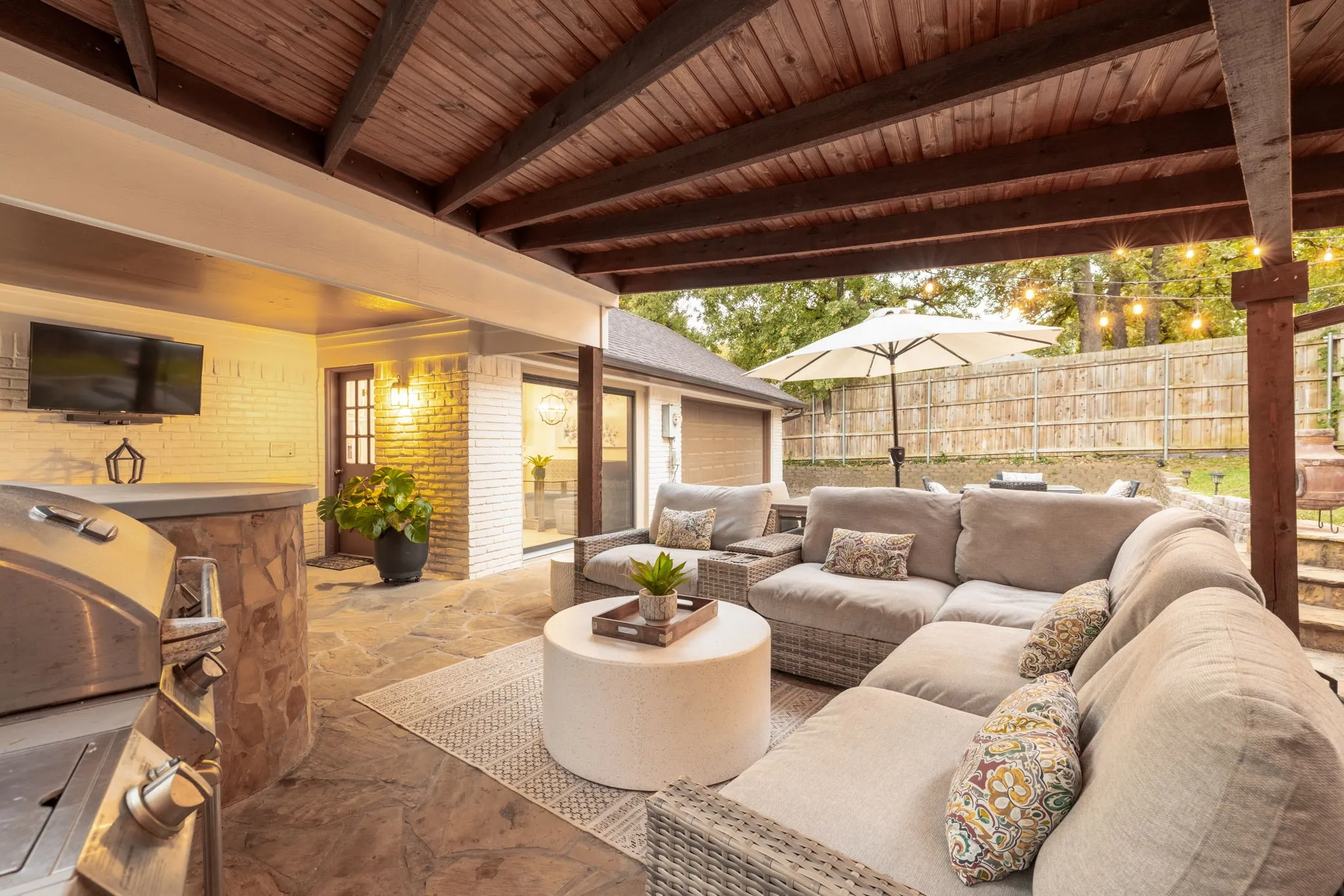 Covered patio featuring a wood-paneled ceiling, stone flooring, and a built-in outdoor grill station with a stone facade