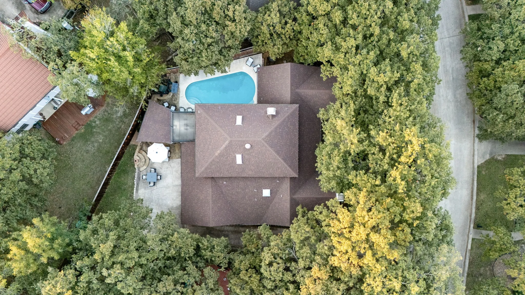 Shingle roof residence surrounded by mature trees, featuring a backyard pool and paved patio