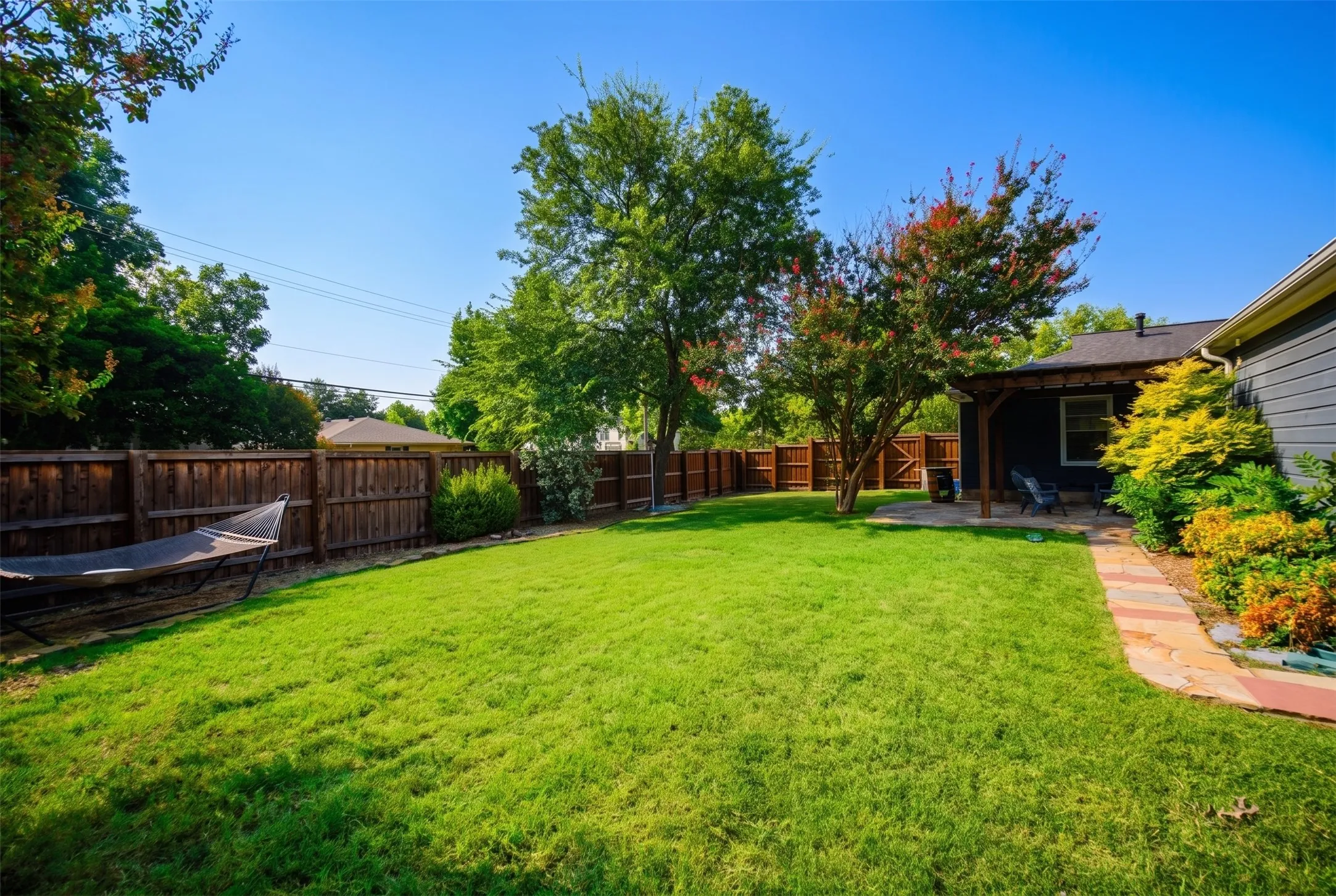 Expansive fenced backyard featuring mature trees, a stone pathway, and a covered patio structure