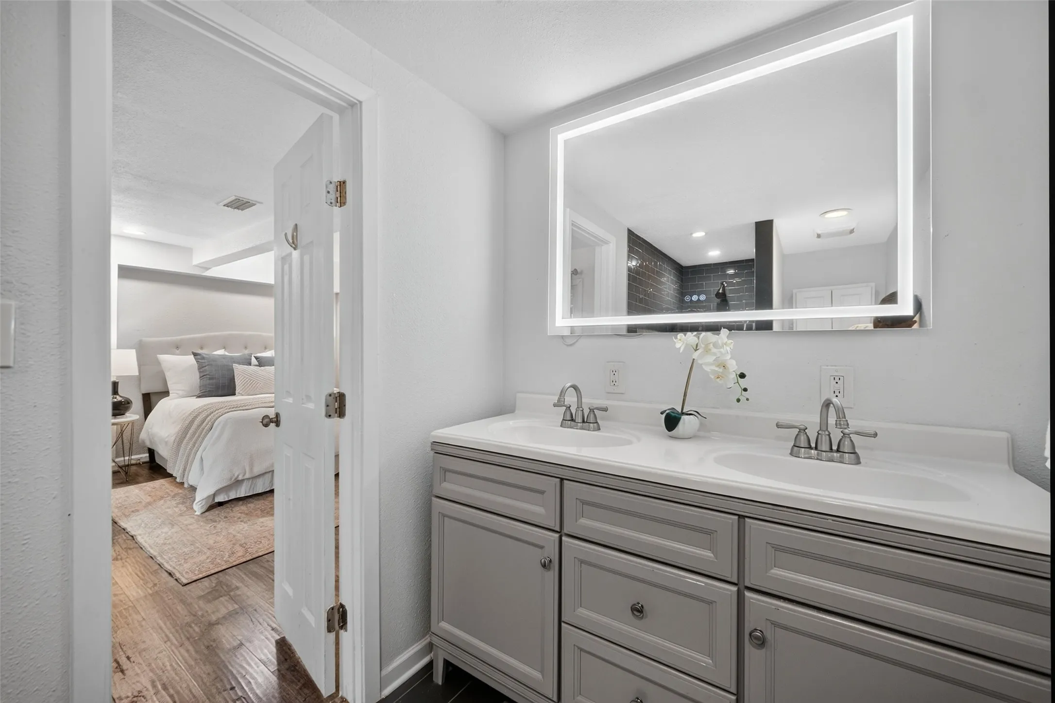 Double vanity with integrated sinks, modern illuminated mirror, and gray cabinetry