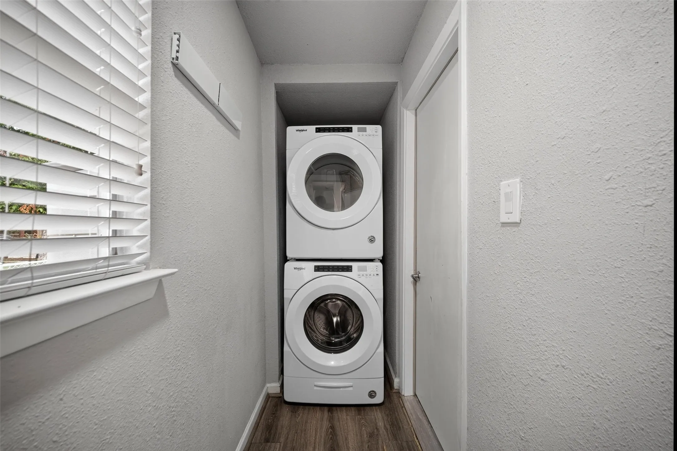 Dedicated laundry area featuring a stacked washer and dryer, wood-finish flooring, and window with blinds
