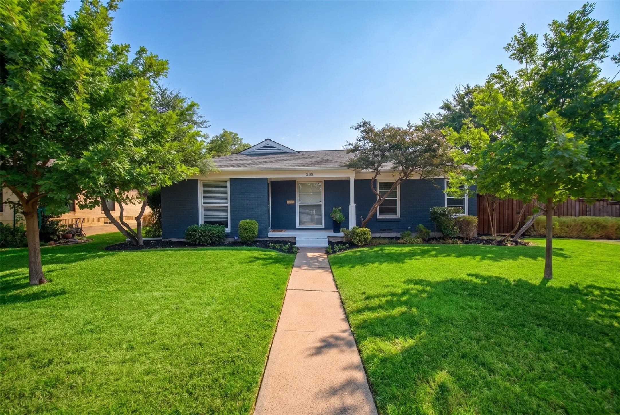 Expansive front lawn with mature shade trees, a concrete pathway, and a covered porch entry featuring white columns