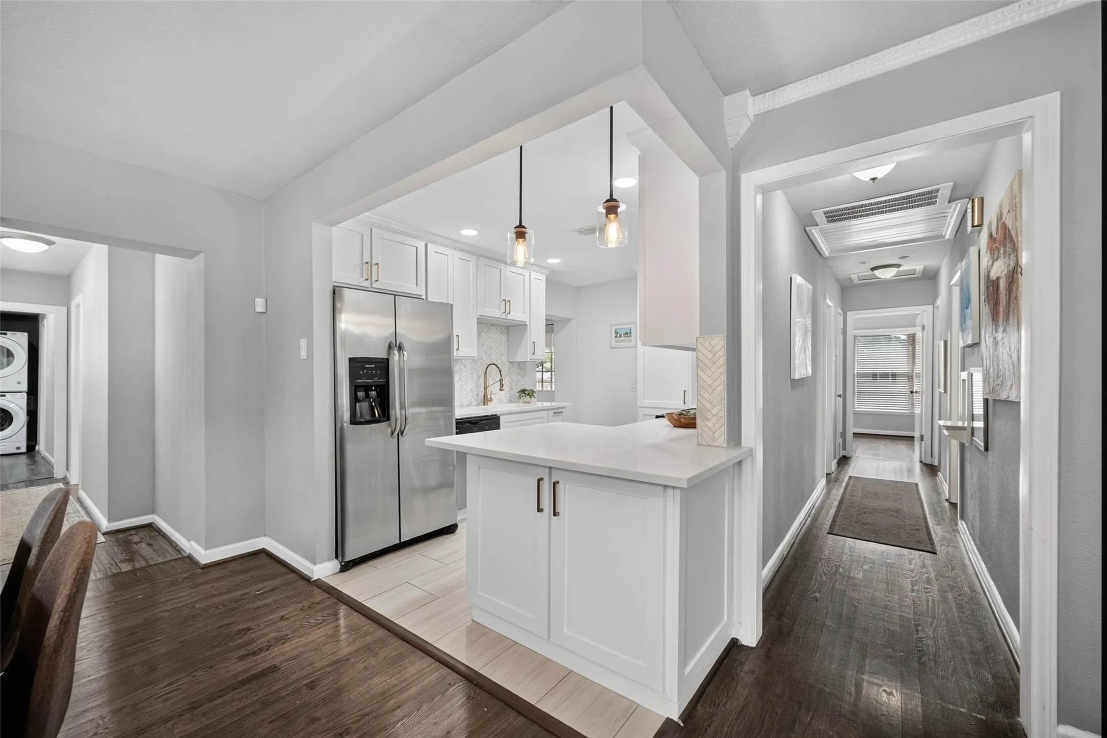 Open-concept kitchen with white cabinetry, stainless steel refrigerator, and pendant lighting