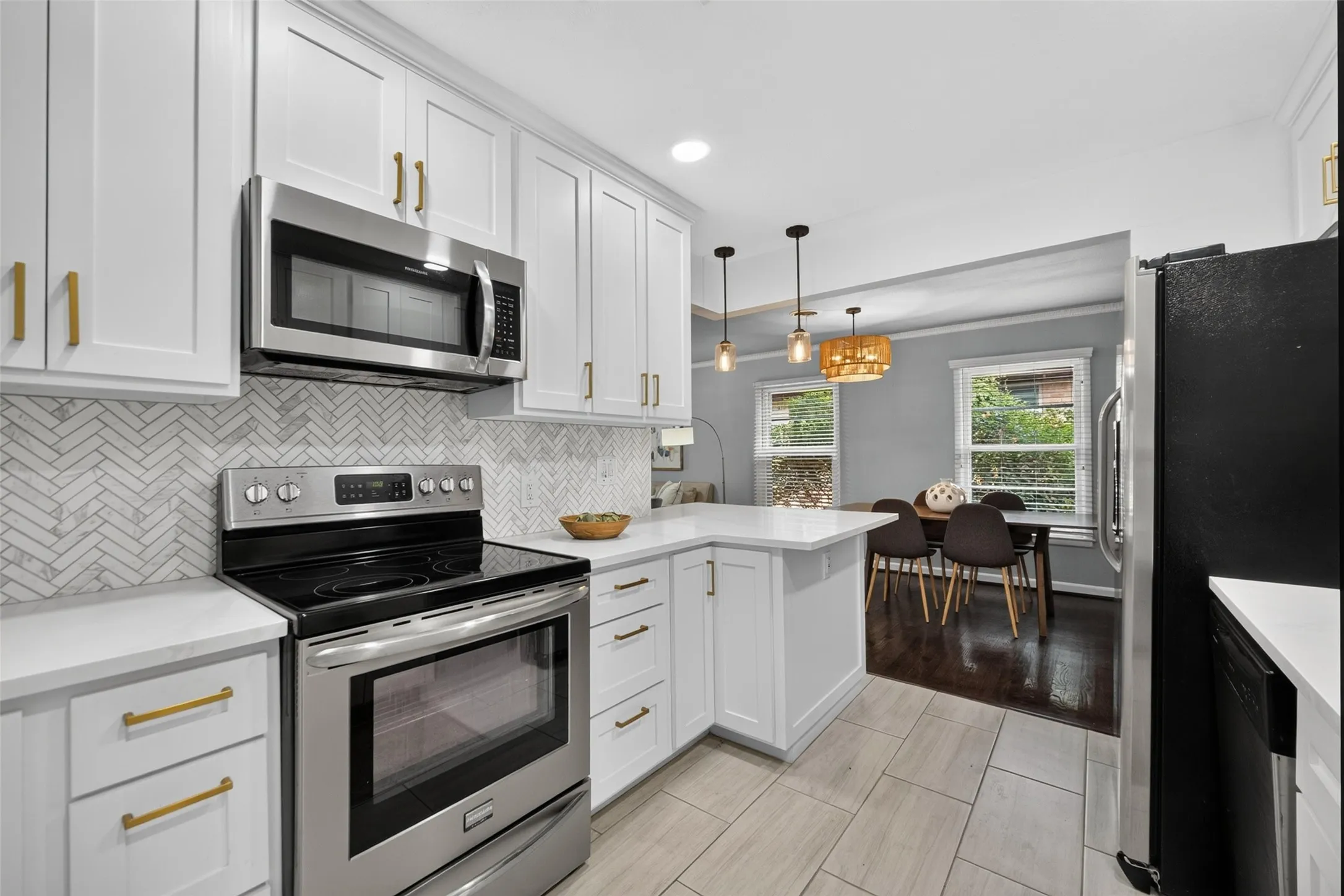 White shaker cabinetry with gold-tone hardware, stainless steel appliances, white herringbone tile backsplash, and light-toned tile flooring