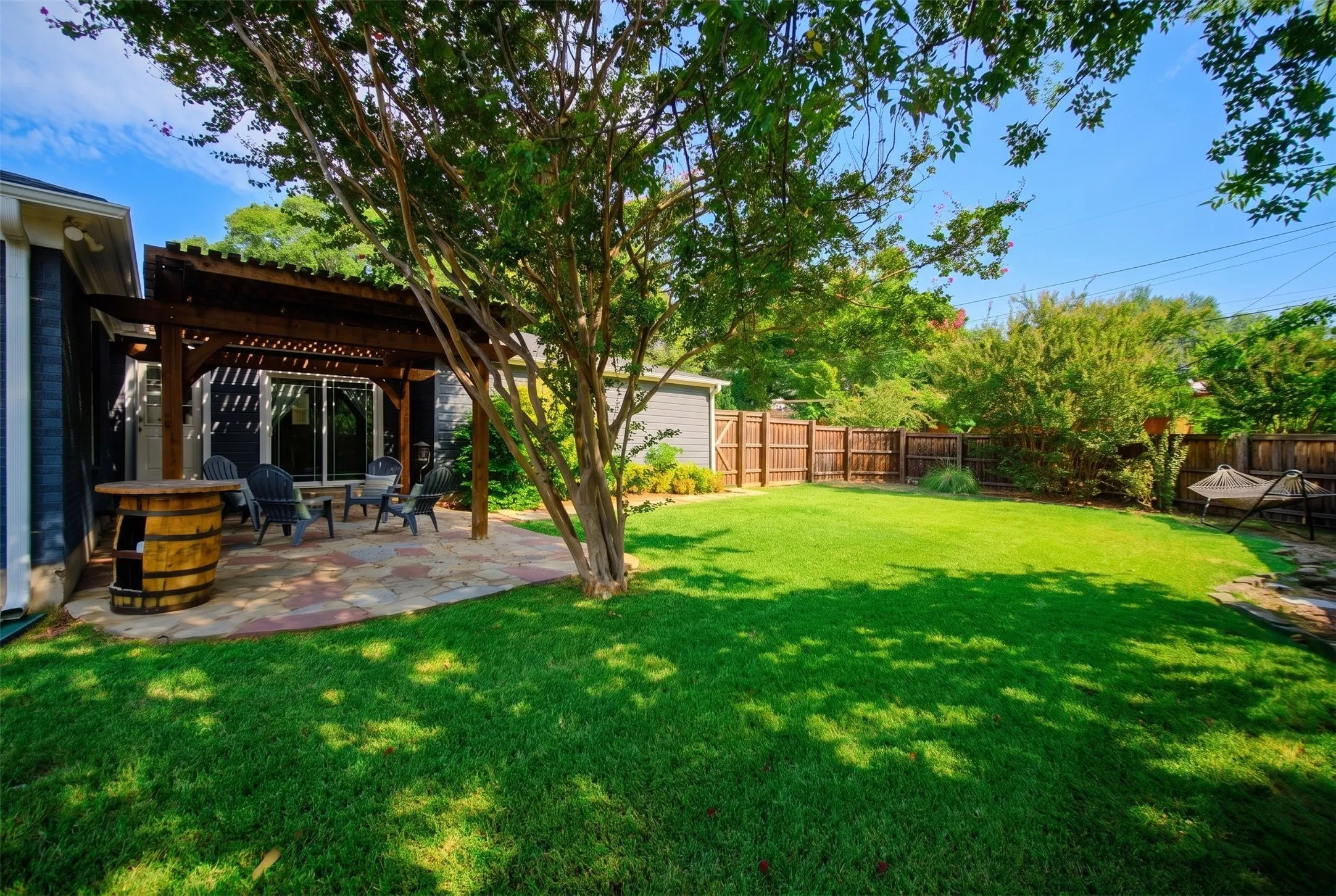 Expansive backyard featuring a lush lawn, a stone patio, a wooden pergola, and mature trees