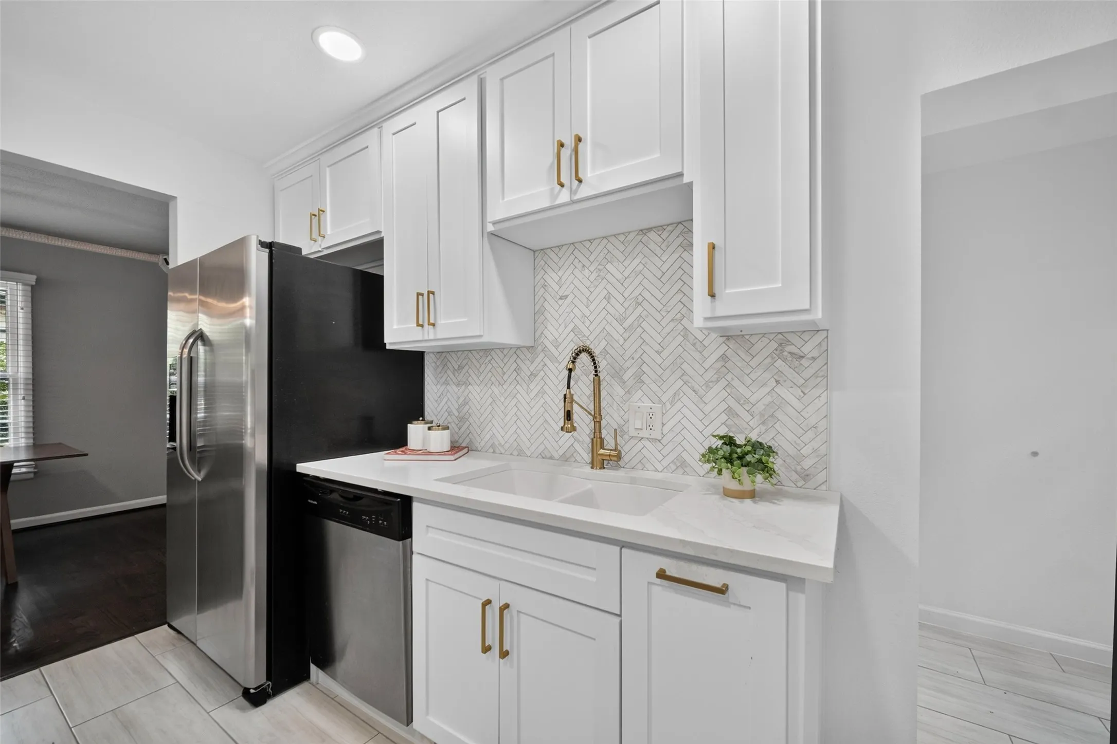 White cabinetry with gold-finish hardware, herringbone tile backsplash, dual basin sink, stainless steel dishwasher, and recessed lighting