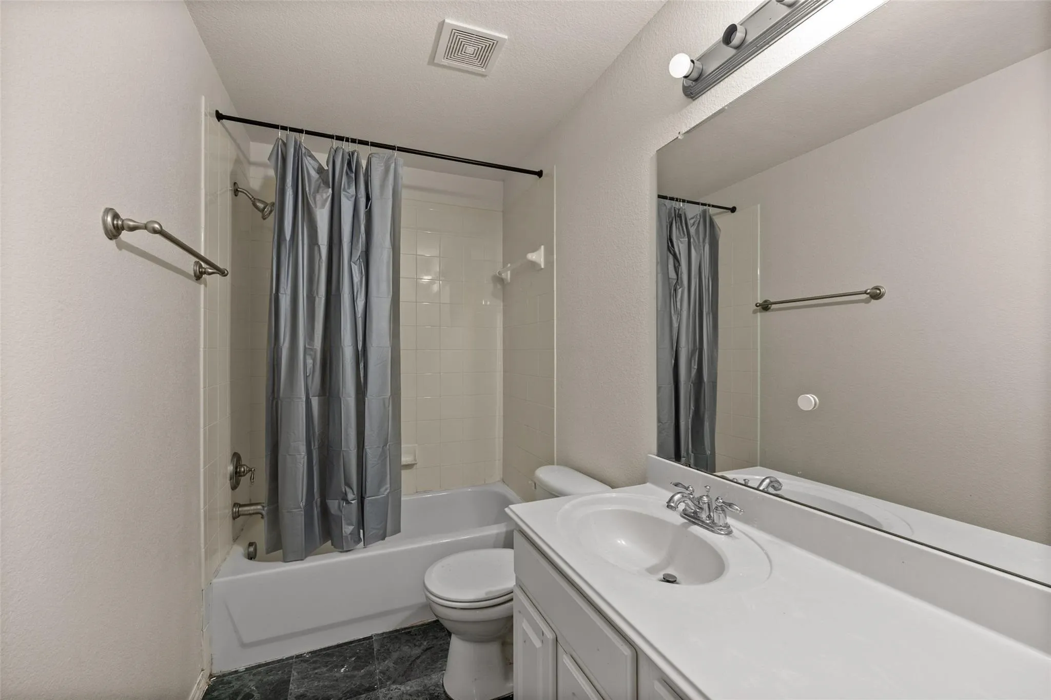 Bathroom featuring a white vanity with integrated sink, a large wall-mounted mirror, a bathtub with white subway tile surround, and dark-toned flooring