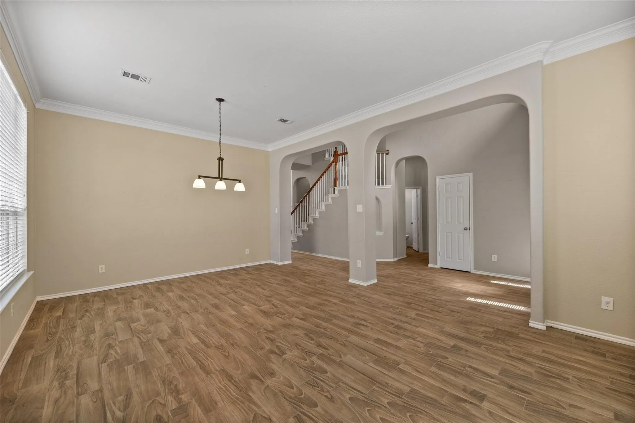 Open concept living space featuring wood-finish flooring, architectural archways, crown molding, a modern chandelier, and a prominent staircase