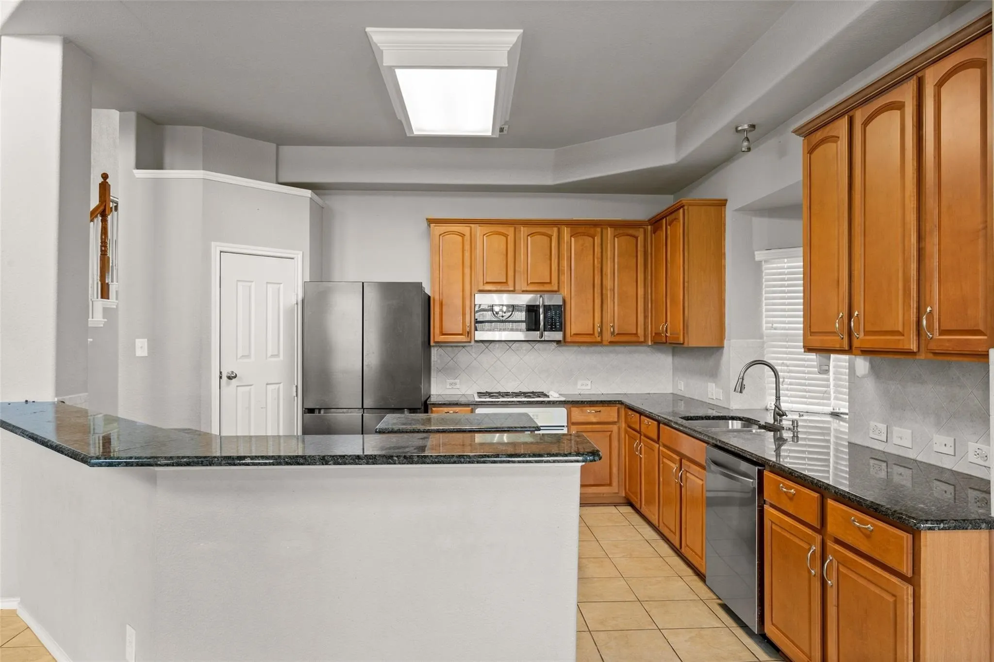 Full kitchen featuring wood cabinetry, stainless steel appliances, dark stone countertops, and tile flooring