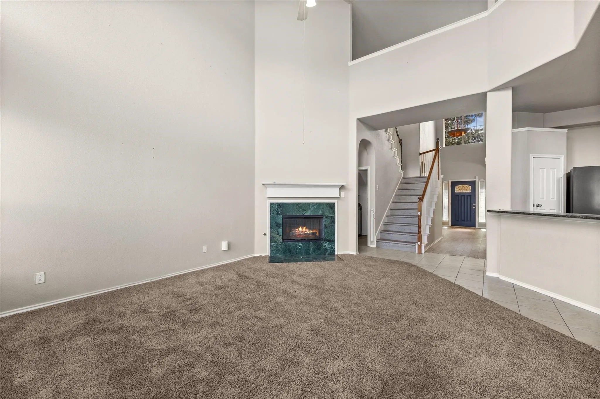 Two-story living area featuring a fireplace with a green surround, carpeted flooring, and high ceilings