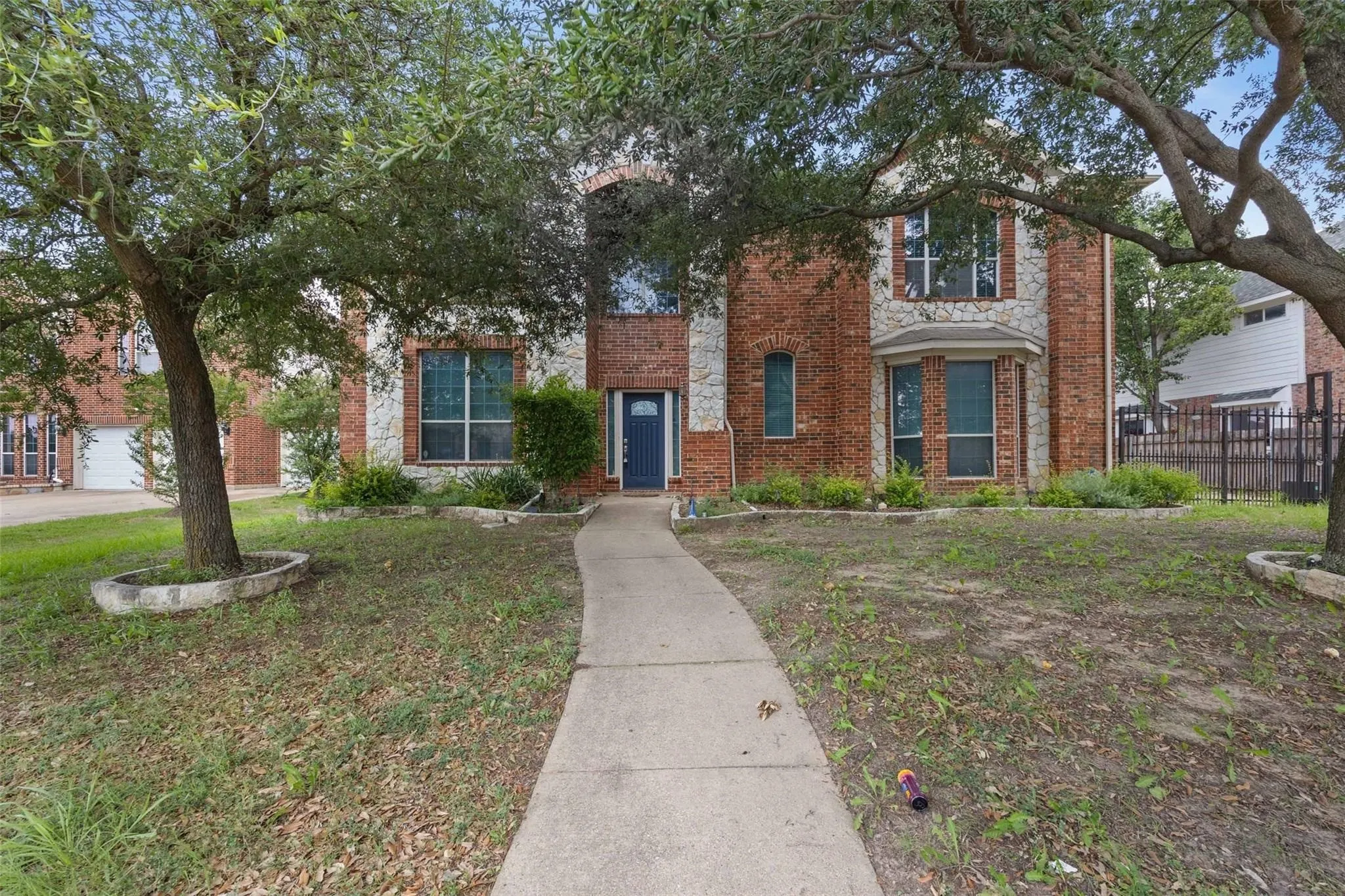 Brick and stone facade, arched entryway, bay window, mature trees, concrete pathway