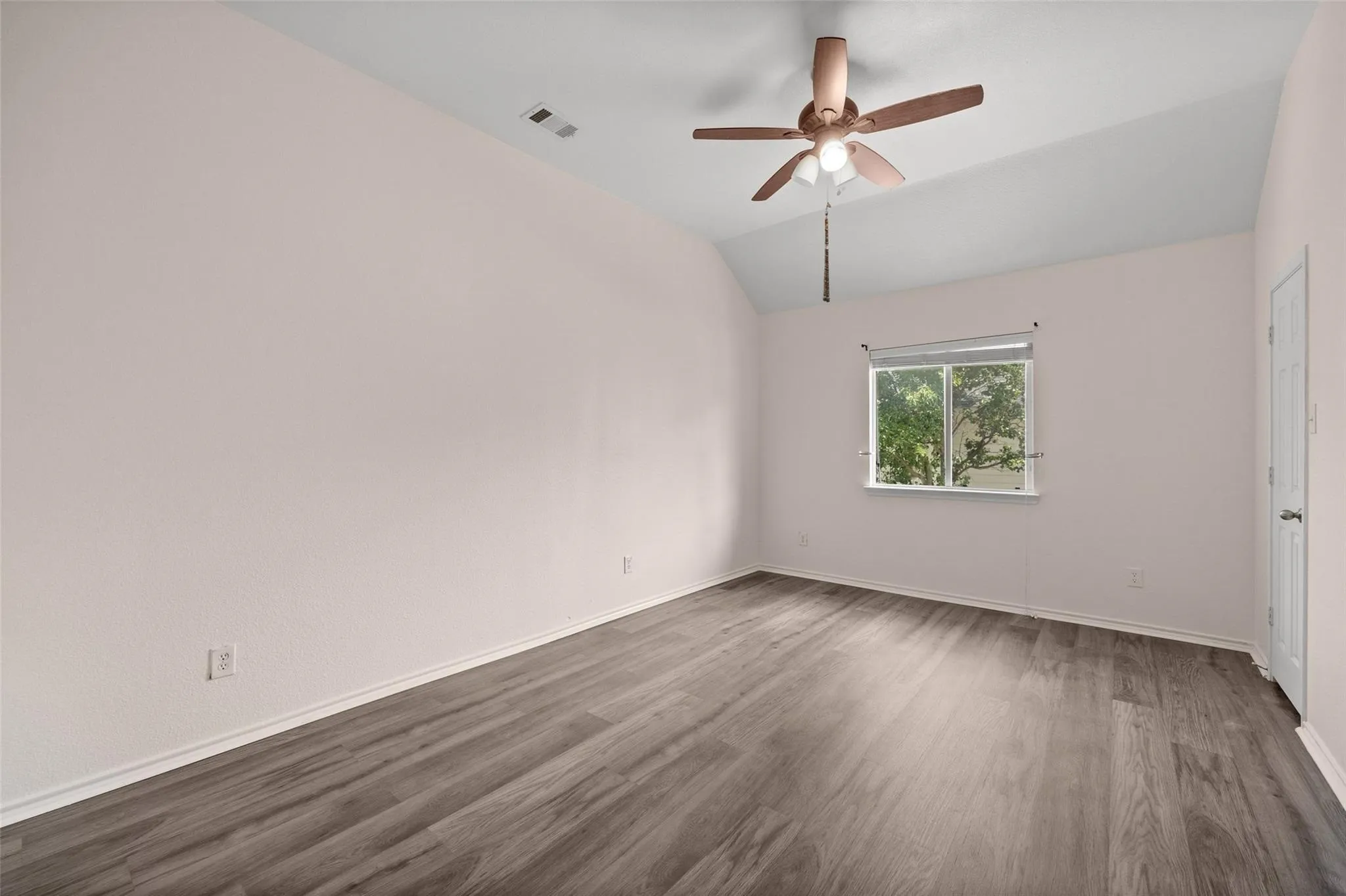 Vaulted ceiling with an integrated ceiling fan, wood-finish flooring, and a window with white trim