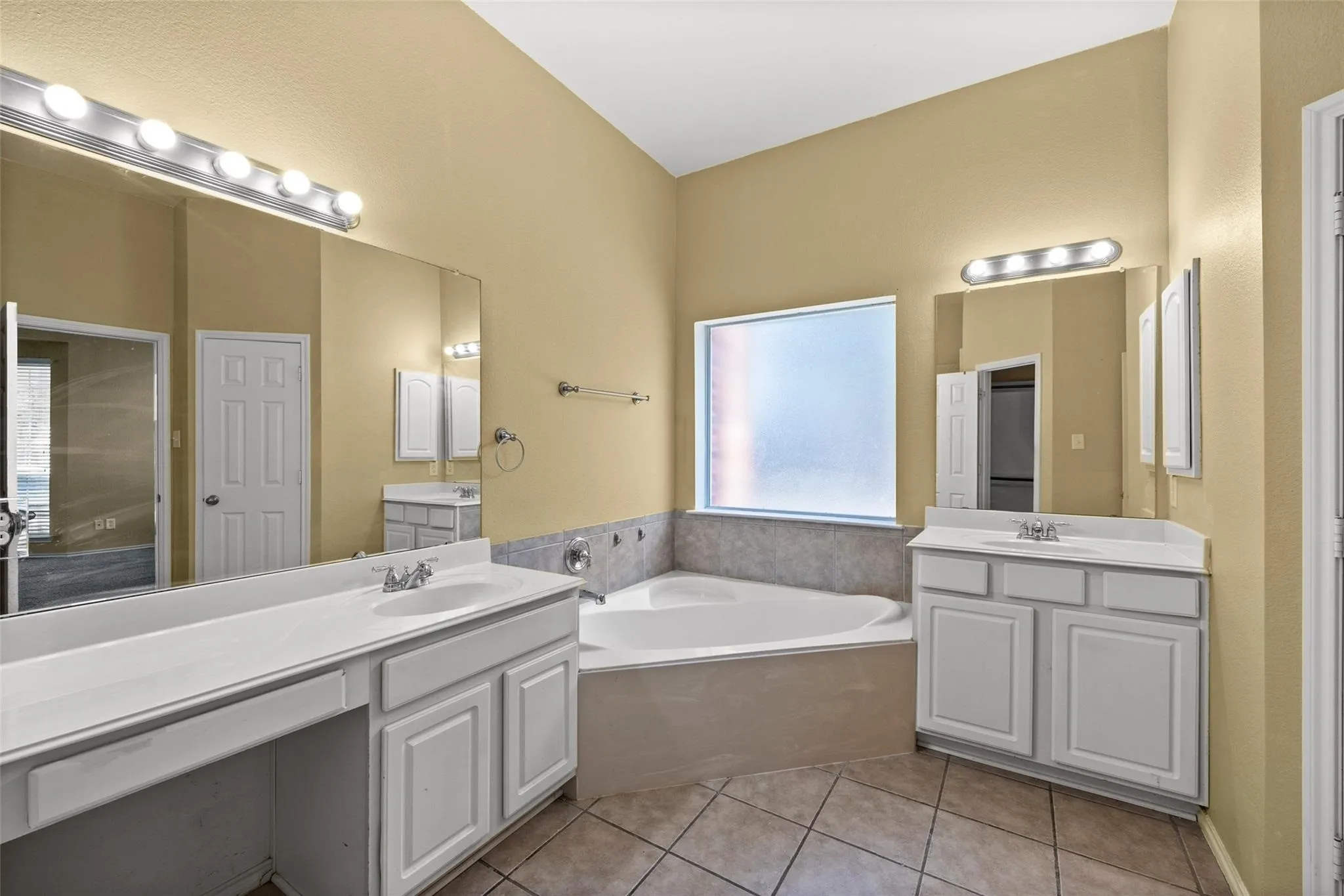 Vaulted ceiling, corner soaking tub, dual vanities, mirrored wall, and tiled flooring