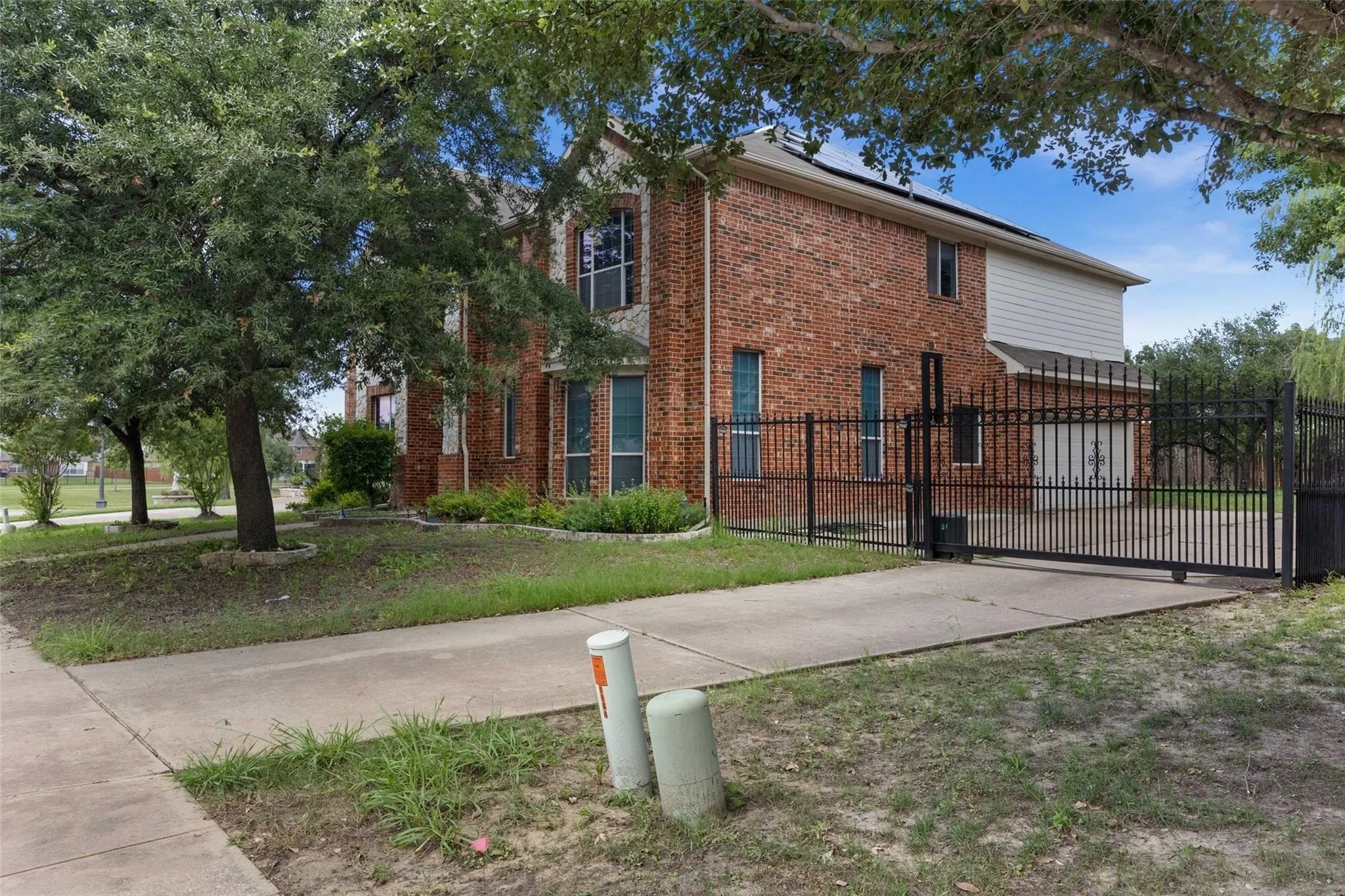 Brick exterior, mature trees, automated metal gate, concrete driveway, and solar panels