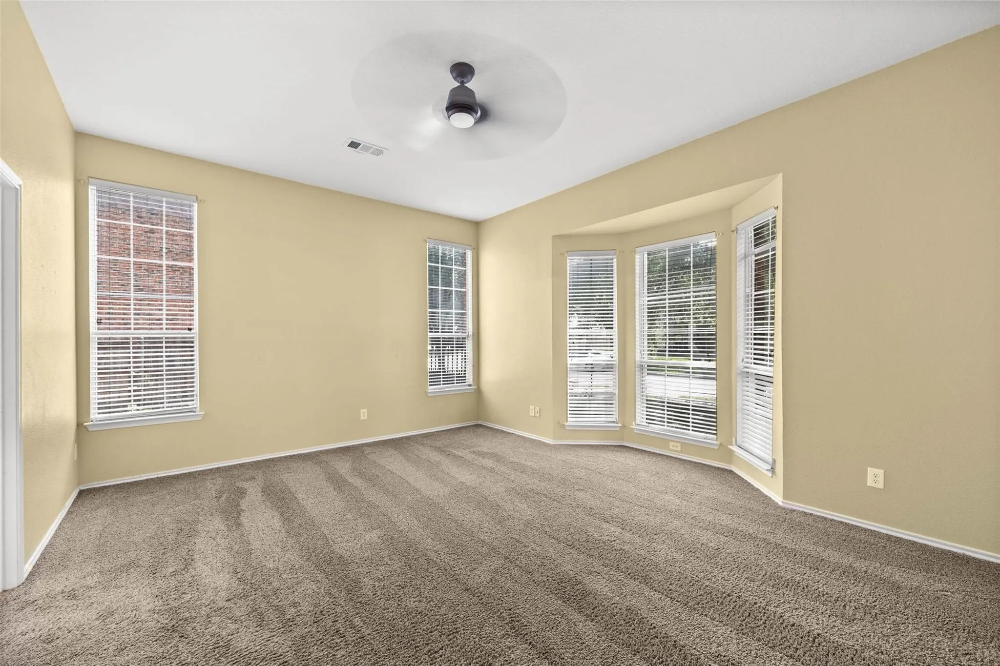 Room featuring neutral carpeting, a bay window with blinds, multiple additional windows with blinds, a ceiling fan, and light-toned walls