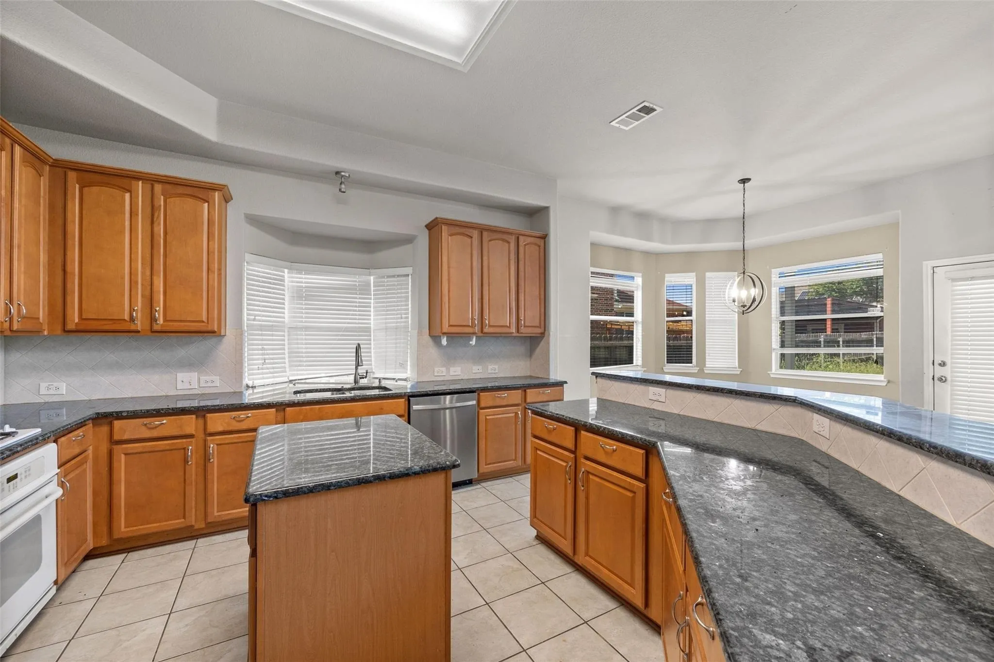 Kitchen featuring wood cabinetry, dark stone countertops, stainless steel appliances, a center island, and tile flooring