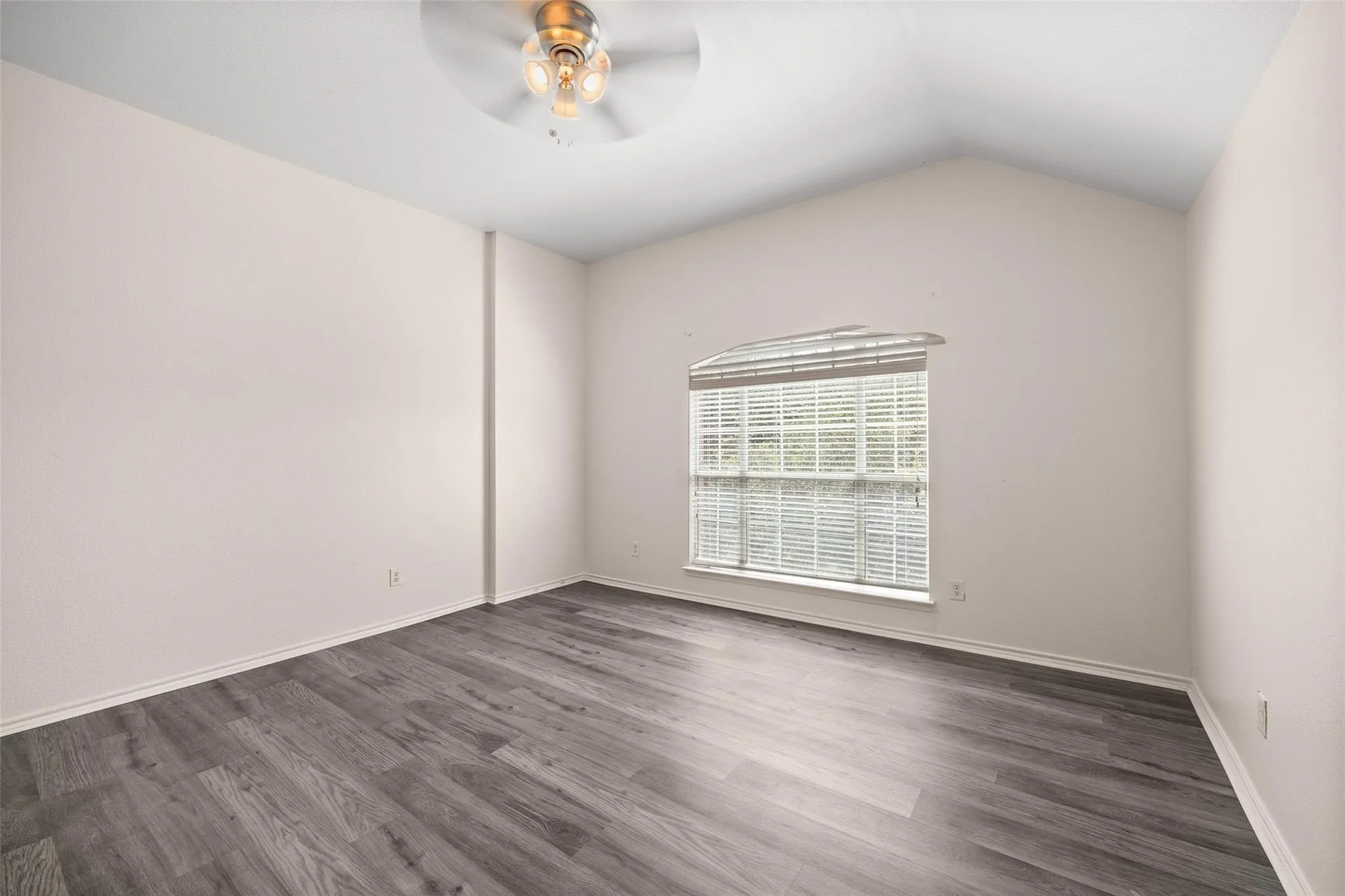 Vaulted ceiling with a ceiling fan, arched window with horizontal blinds, and wood-finish flooring